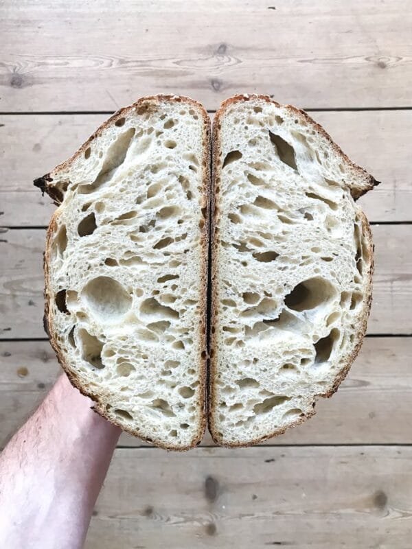 From above of anonymous person with halves of delicious fresh sourdough on hand standing on wooden floor in light room